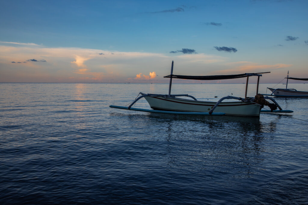 Blue hour over calm ocean and black sand beach with balinese boat
