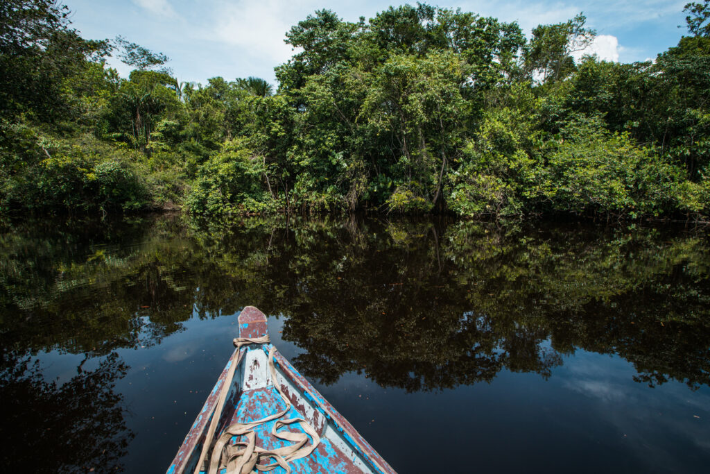 An open wooden boat floating on a brown tropical river, Guyana, South America.