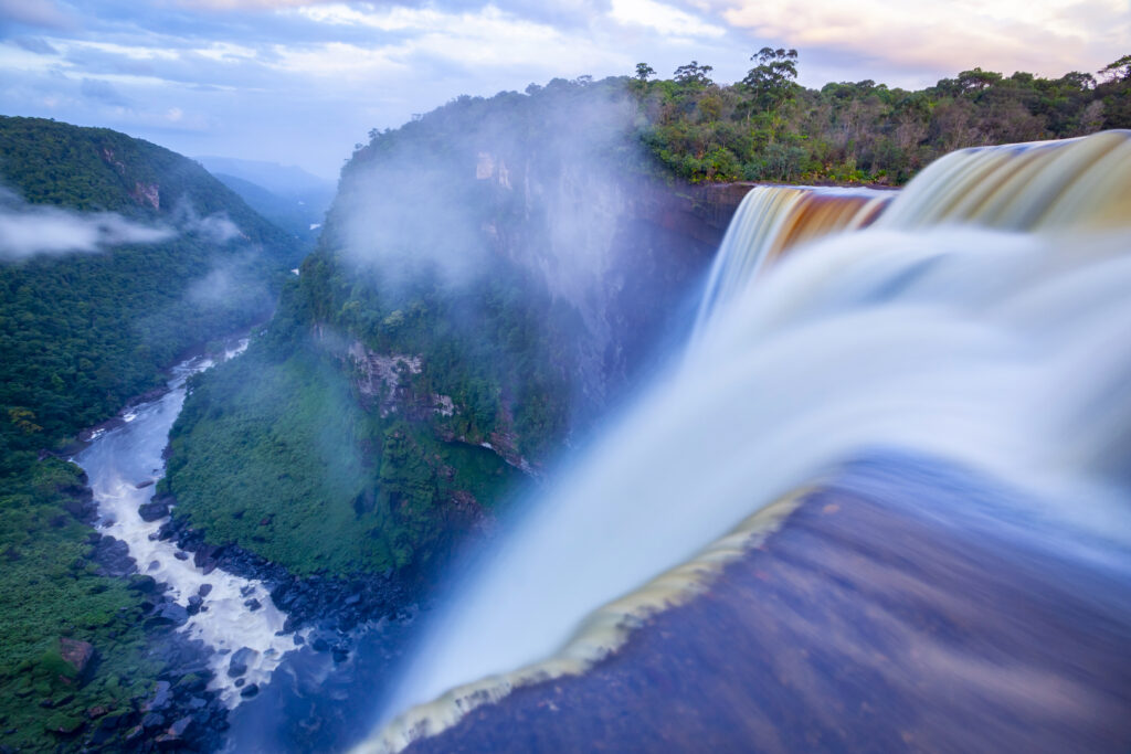 Long exposure shot of water flowing over the edge of Kaieteur Falls into the Potaro River valley in evening light after sunset, Kaieteur National Park, Potaro-Siparuni region, Essequibo territory, Guyana. Kaieteur Falls are considered the largest single-drop waterfall in the world. The Essequibo region is the subject of a dispute between Guyana and Venezuela.